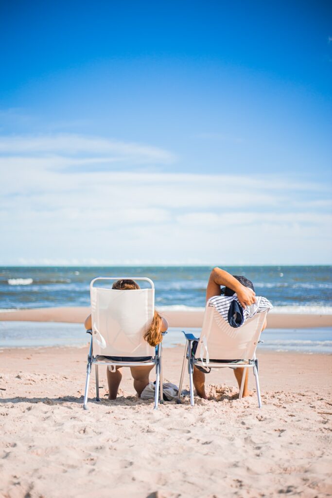 vrouw in zwart-wit gestreepte jurk zittend op een witte stoel op het strand overdag